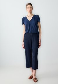 T-shirt marine à col en V en tissu doux associé à un pantalon cropped texturé marine, présentant une coupe décontractée et des sandales ouvertes marron.