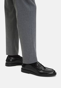 Czarne skórzane mokasyny o gładkim wykończeniu i widocznym szwie, w połączeniu z szarymi spodniami, prezentując elegancki, klasyczny design.