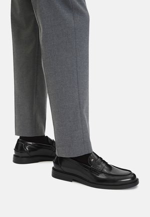 Czarne skórzane mokasyny o gładkim wykończeniu i widocznym szwie, w połączeniu z szarymi spodniami, prezentując elegancki, klasyczny design.