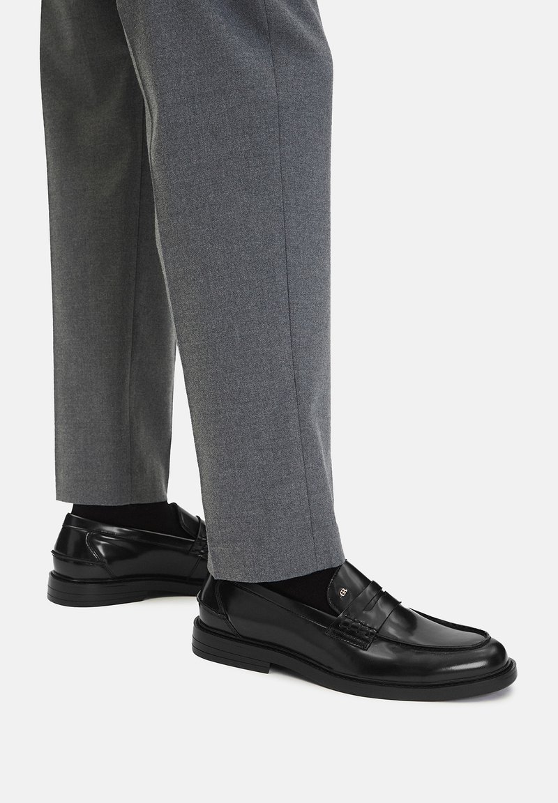 Czarne skórzane mokasyny o gładkim wykończeniu i widocznym szwie, w połączeniu z szarymi spodniami, prezentując elegancki, klasyczny design.