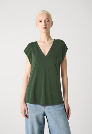 Maglietta verde con scollo a V, maniche corte e vestibilità comoda, realizzata in tessuto morbido; abbinata a jeans larghi in denim chiaro.