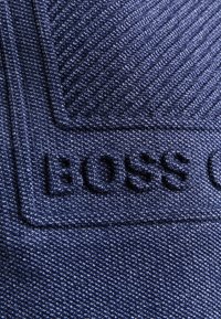 Námořnicky modrá textilie s texturovaným vzorem. Obsahuje vystouplé písmo "BOSS" v kontrastním designu a jemný diagonální vzor tkaní.