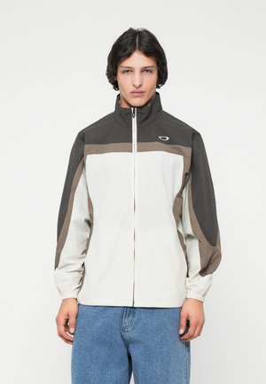 Veste légère bicolore avec un col montant. Comprend des panneaux gris et beige, des poignets élastiques et une fermeture éclair sur le devant. Texture de tissu durable.