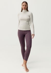 Form-fitting svetložltý top s dlhými rukávmi a vysokým golierom, doplnený temnopurpurovými legínami s jemným opakujúcim sa vzorom.