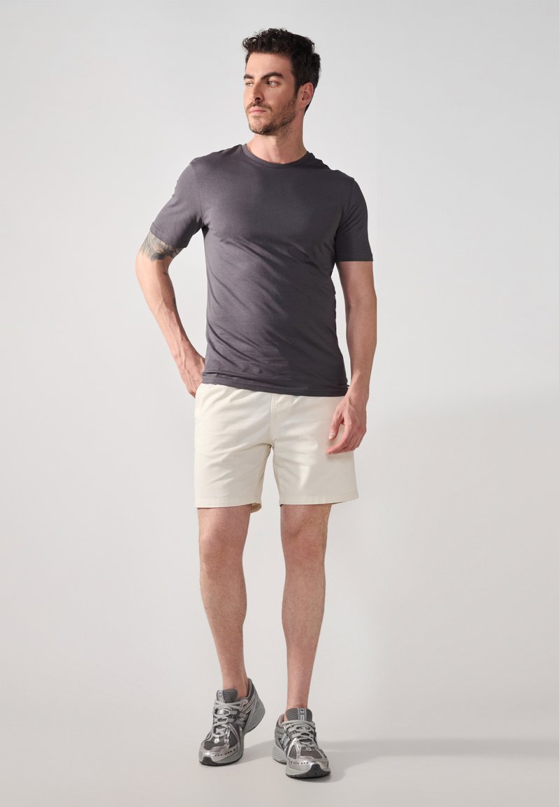 Grijs T-shirt met korte mouwen, gecombineerd met lichte beige shorts en grijze sneakers. De stof lijkt glad, met een aansluitend ontwerp en subtiele details.
