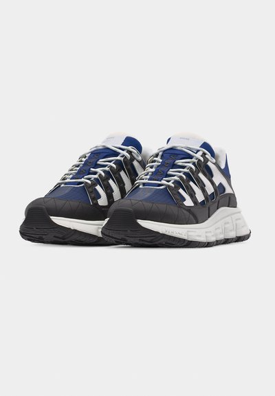 Ζευγάρι αθλητικά παπούτσια σε μπλε, μαύρο και λευκό χρώμα με χοντρές σόλες και εκλεπτυσμένο δέσιμο κορδονιών, τοποθετημένα δίπλα-δίπλα σε απλό φόντο.