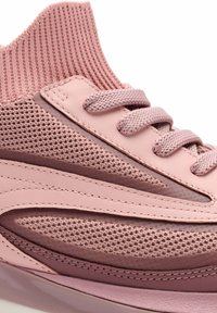 Primer plano de una zapatilla rosa con un cuello de punto texturizado en el tobillo, cordones trenzados y paneles superpuestos de malla y cuero sintético.