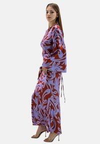 Vestido maxi en rojo y lila con patrones florales. Mangas largas y cintas en la cintura. Tela suave con una silueta fluida y abertura.