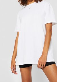 Bílá bavlněná tričko s uvolněným střihem, kulatým výstřihem a krátkými rukávy. Má rovný lem a minimalistický design.