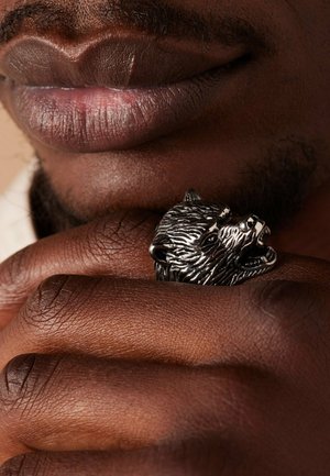 Sterling silver bear head ring rests on dark skin, showcasing intricate detailing in the fur and facial features. Smooth texture, bold design.