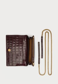 Tummanruskea krokotiilinkoipaisen nahkalompakko, jossa on kultainen painonappi, auki oleva vetoketjullinen osasto ja irrotettava kultaketju valkoisella taustalla.