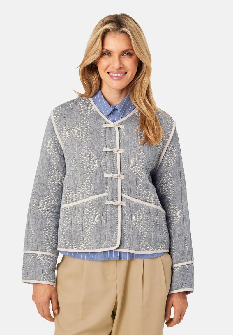 Blaue gemusterte Jacke mit weißen Akzenten, aus strukturiertem Material, mit Stehkragen und traditionellen geknoteten Verschlüssen.