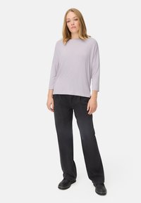 Lichtpaarse, lange mouw shirt met een ronde halslijn, gecombineerd met losse zwarte broeken. Model staat tegen een effen achtergrond. Eenvoudig ontwerp.