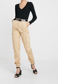 Svart ribbad långärmad V-ringad topp i kombination med beigefärgade cargobyxor med elastiska cuffs och sidofickor, kompletterad med ett brett svart bälte och klacksandaler.