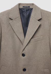 Cappotto in misto lana marrone con rever, monopetto con due bottoni neri, taschino sul petto e una fodera nera liscia.