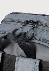 Zaino in tessuto grigio con doppia zip, dotato di accessori neri, superficie testurizzata e spallacci resistenti. Primo piano del dettaglio della zip.