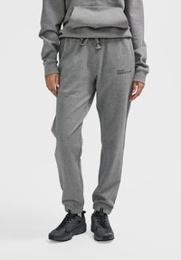 Graue Sweatpants aus weichem Stoff, mit einem Kordelzugbund, seitlichen Taschen und "HALO 1968197291981" auf dem linken Oberschenkel bedruckt.