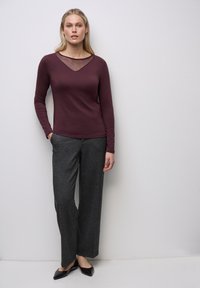 Top bordeaux a maniche lunghe con scollatura a V trasparente e pantaloni grigi a gamba larga. Tessuto morbido con una sottile texture e scarpe scure e lucide.