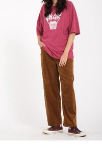 Overdimensioneret, falmet magenta t-shirt med hvid grafik; brun fløjl brede bukser; maroon sneakers med hvide detaljer.