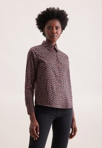 Camicia a maniche lunghe in tessuto marrone scuro con motivo floreale nei toni del rosa e dell'arancione; presenta una chiusura con bottoni e colletto.