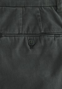 Schwarzer Stoff mit glatter Textur, ausgestattet mit einem einzelnen schwarzen Knopf und genähten Details an der Taille, mit Falten für das Design.