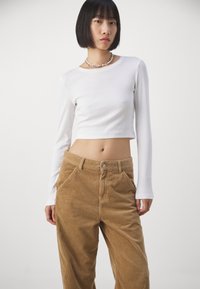 Crop top blanc à manches longues avec un design ajusté, associé à un pantalon en corduroy beige taille haute avec une finition texturée et des poches avant.