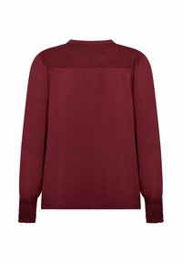 Bordeaux lange mouwtop met een smockede achterpas en gathers aan de mouwen. De stof lijkt zacht met een gladde textuur en heeft een relaxed fit.