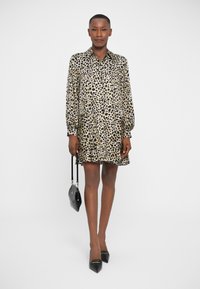 Vestido de estampado de leopardo con mangas largas, cuello y dobladillo acampanado; hecho de una tela suave y lisa. Tacones negros de punta y un bolso pequeño.