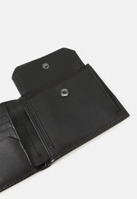 Interior de una cartera de cuero negro con cierre a presión, ranuras para tarjetas y un acabado suave. Costuras detalladas y elementos de diseño minimalistas.