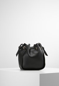 Svart läderhinkväska med rund form, dragsko upptill och detaljer i guldton. Har dubbla axelremmar och en texturerad yta.