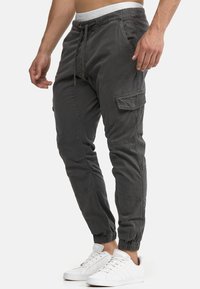 Graue Cargo-Jogginghosen mit elastischem Bund und Kordelzug, ausgestattet mit Seitentaschen und elastischen Bündchen an den Knöcheln. Getragen mit weißen Sneakers.