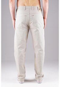 Beige Hosen mit geradem Schnitt, fünf Taschen, Metallnieten und einem Markenpatch am Bund. Glatte Stofftextur.