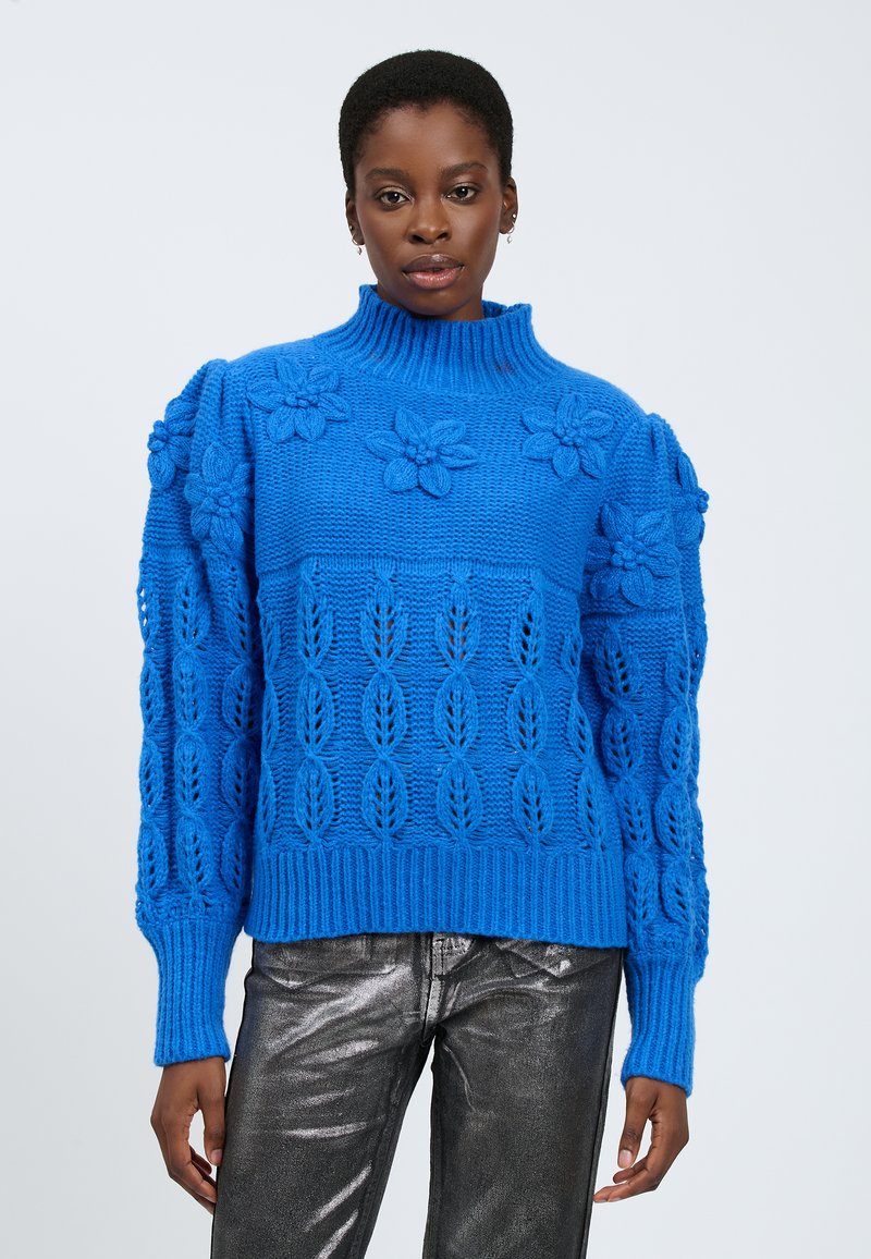 Maglione blu lavorato a maglia con collo alto, caratterizzato da motivi floreali e fogliari, polsini e orlo a coste, e una finitura testurizzata. Abbinato a pantaloni metallici argento.