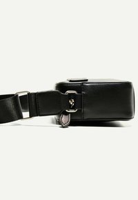 Crna kožna torbica za crossbody s pravokutnim oblikom. Ima podesivu traku, srebrne hardverske dijelove i suptilan oznaku naglašenu sa strane.