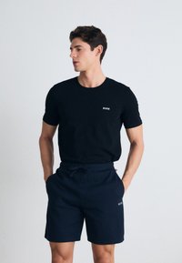 Camiseta de algodón negra con mangas cortas y logotipo blanco "BOSS", combinada con pantalones cortos azul marino que cuentan con una cintura elástica y cordón.