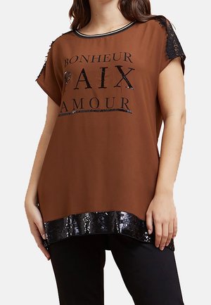 Bruine top met korte mouwen, zwarte kanten schouderdetail, zwarte paillettenzoom en zwarte Franse woorden "Bonheur Paix Amour" over de borst.