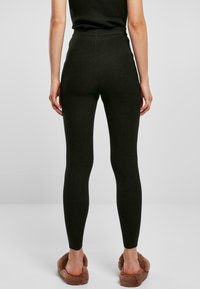 Ribbad mörkgrön leggings med hög midja, smal passform och textilstruktur, i par med ljusbruna fluffiga tofflor.