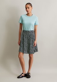 Lichtblauw T-shirt met korte mouwen gecombineerd met een donker gestippelde uitlopende rok. Zwarte sandaaltjes met bandjes maken de outfit compleet. Glad textiel is zichtbaar.
