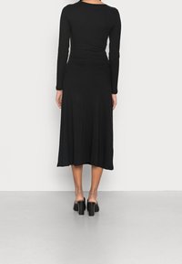 Musta ribbed pitkähihaista mekkoa, jossa on istuva yläosa ja lainehtiva midi-pituinen hame. Ominaisuuksiin kuuluu pyöreä pääntie ja sileä pinta.