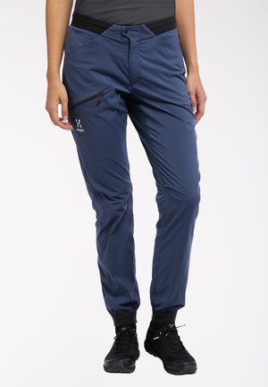 Navy waterproof hiking pants with a slim fit, zippered thigh pocket, elastic waistband, and elasticized cuffs for adjustable fit.