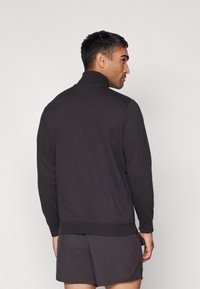Sweat à zip noir avec un col montant, fabriqué en tissu doux. Présente une coupe décontractée et des poignets côtelés, associé à un short assorti.
