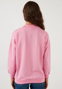 Felpa rosa con scollo rotondo, maniche lunghe e polsini a costine. Tessuto morbido con una vestibilità rilassata e texture liscia.