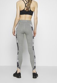 Leggings grigi con un design aderente, caratterizzati da un motivo grafico in bianco e nero lungo i lati e una texture liscia e elastica.