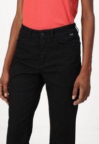 Schwarze Jeans mit einer glatten Textur, ausgestattet mit fünf Taschen, einem Knopfverschluss und subtilen Hardware-Akzenten.