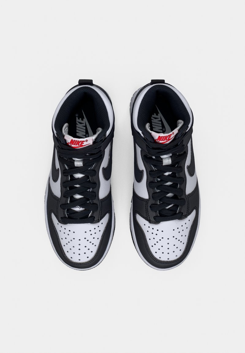 Baskets montantes Nike avec un design en cuir noir et blanc, bout perforé, doublure en tissu texturé, et accents rouges sur le logo.