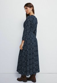 Navy-blaues Maxikleid mit langen Ärmeln, floralem Muster und Rüschenausschnitt. Tailliert mit fließendem Rock, kombiniert mit braunen Ankle-Boots.