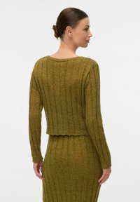 Olivgrön ribbad stickad tröja med långa ärmar, kort design och rundad halsringning. Slät textur och ojämn fålldetalj.