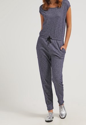 Tuta blu navy con maniche corte, vita elasticizzata e coulisse. Presenta tasche laterali e una vestibilità comoda, abbinata a scarpe argento.