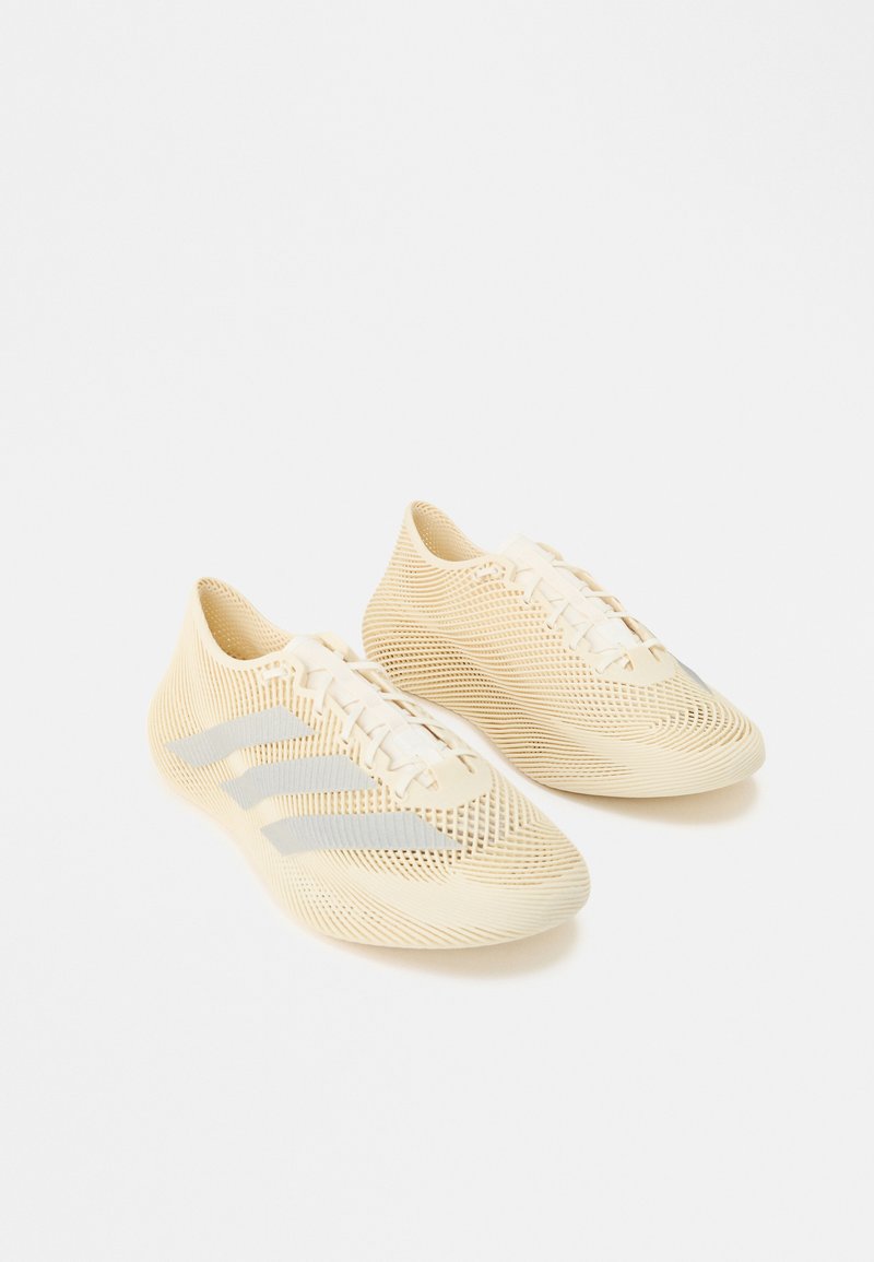 Chaussures de sport légères beiges avec surface texturée, design à lacets et trois bandes gris clair sur le côté.