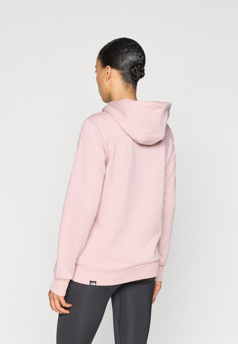 Lyserød hættetrøje med snøre i hætten, ribbede manchetter og en logomærkat nær kanten. Glat stoftekstur, afslappet pasform, minimalistisk design.